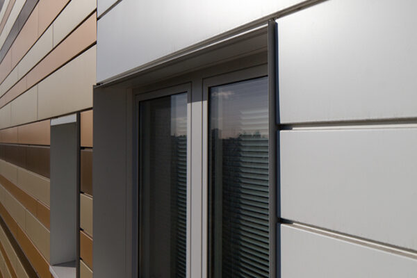 Fenster in einer modernen Fassade mit glänzenden, farbigen Metallpaneelen und horizontalen Linien.