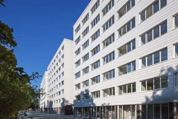 Moderne Wohngebäude mit weißen Fassaden und großen Fenstern, unter blauen Himmel und umgeben von Bäumen.
