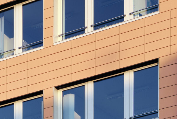 Fassade eines modernen Gebäudes mit großen Fenstern und orangefarbenen Wandplatten.
