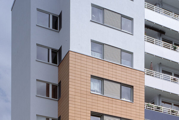 Moderner Wohnblock mit orangefarbenen und weißen Fassadenelementen, mehreren Fenstern und Balkonen.
