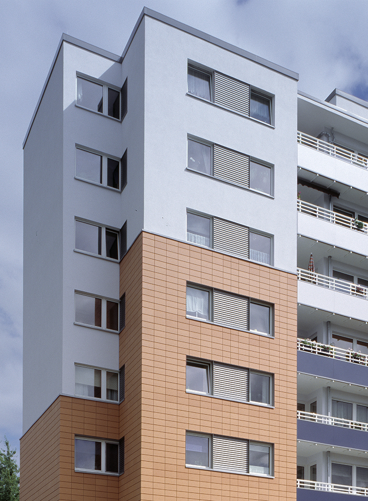 Moderner Wohnblock mit orangefarbenen und weißen Fassadenelementen, mehreren Fenstern und Balkonen.