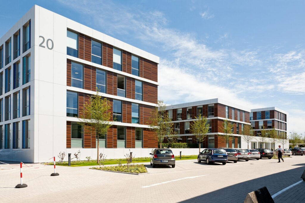 Moderne Bürogebäude mit Holzverkleidung, Parkplatz und Bäumen unter blauem Himmel.