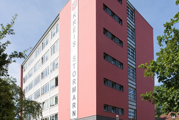 Modernes Gebäude des Kreises Stormarn mit pinker Fassade und großen Fenstern, umgeben von Bäumen und Grünflächen.