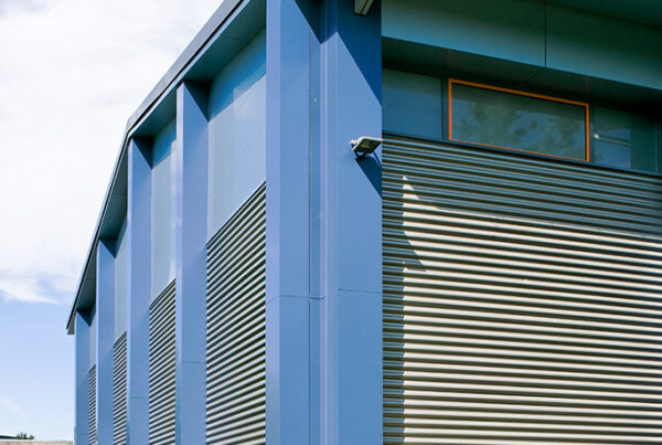 Moderne Industriegebäude mit blauer Fassade und vertikalen Lamellen, umgeben von unberührter Natur und grünem Bewuchs.