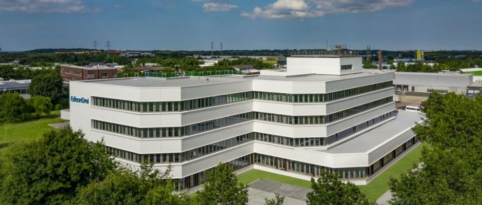 Moderne Firmengebäude mit mehreren Etagen und großen Fenstern, umgeben von Grünflächen und Industrieanlagen.