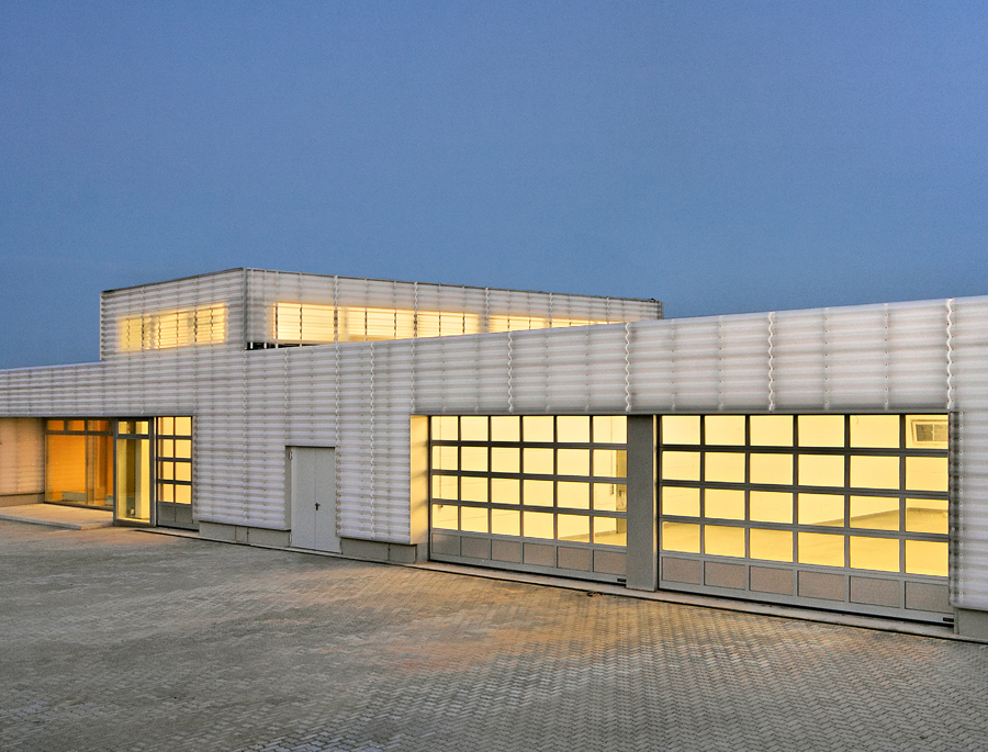 Moderner, lichtdurchfluteter Gebäudekomplex mit großen Fenstern und minimalistischer Architektur bei Dämmerung.