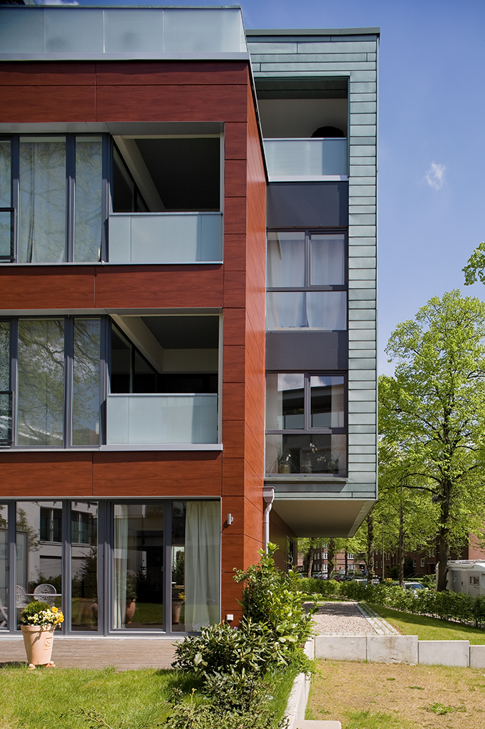 Moderne Wohngebäude mit Holz- und Glasfassade, großen Fenstern und Balkonen, umgeben von Grünflächen.
