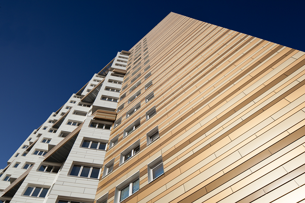 Hochhaus mit moderner Fassade aus goldfarbenen und weißen Platten, aufgenommen aus einem niedrigen Blickwinkel.