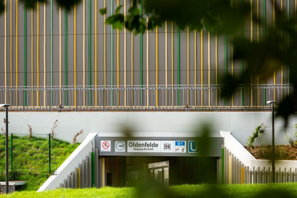 Eingang zur U-Bahn-Station Oldenfelde mit farbiger Fassade und Hinweisschildern für Fahrgäste.