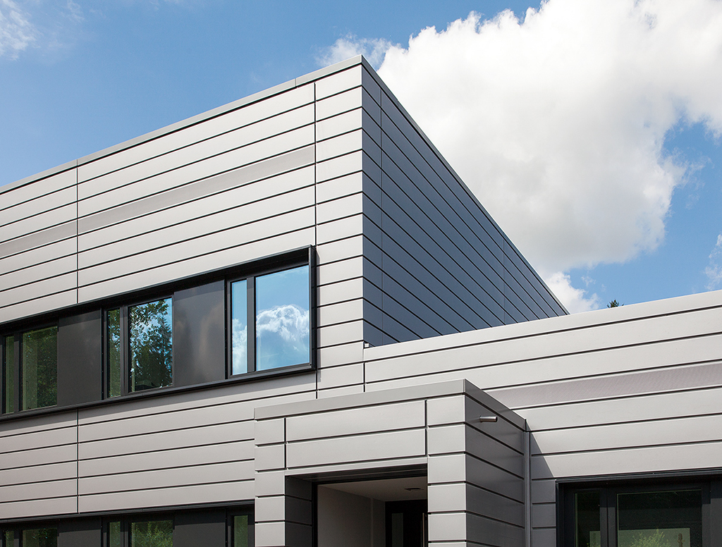 Moderne Architektur mit schlichten, grauen Fassaden und großen Fenstern unter blauem Himmel und weißen Wolken.
