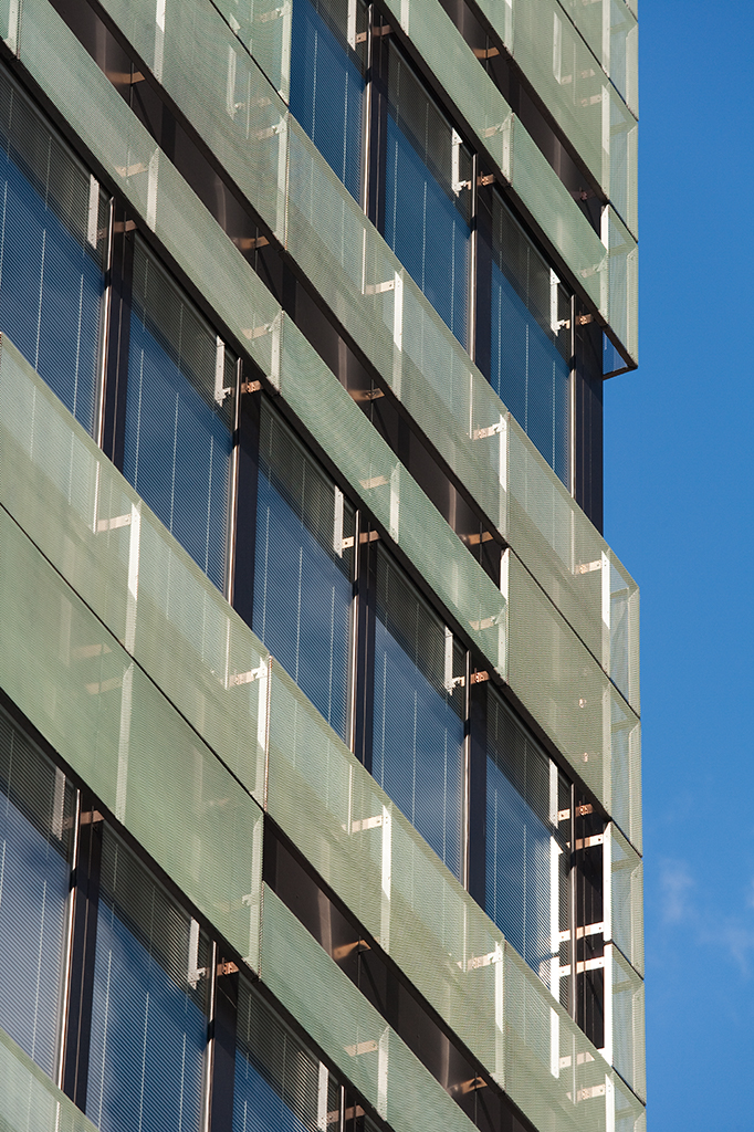 Detailaufnahme einer modernen Gebäude-Fassade mit Glas- und Metall-Elementen vor blauem Himmel.