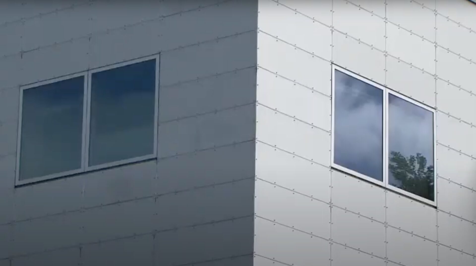 Zwei Fenster an der Ecke eines modernen Gebäudes mit reflektierenden Oberflächen und einer strukturierten Außenwand.